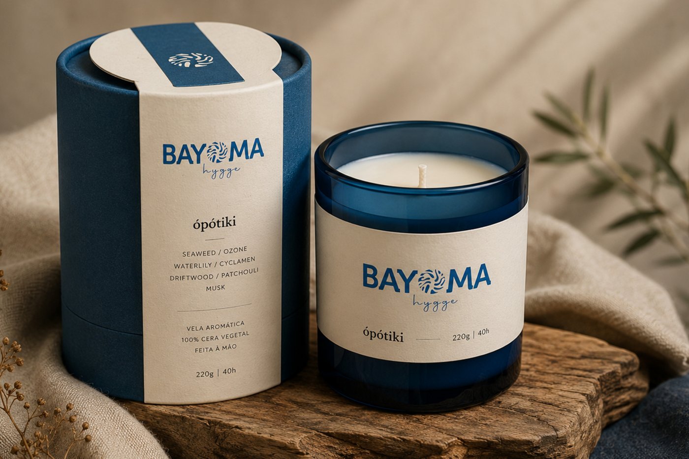 Vela aromática em copo azul-marinho ao lado da embalagem cilíndrica, sobre madeira rústica